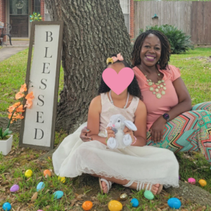 Single foster parent sits under a tree with daughter surrounded by easter eggs and a sign that says blessede